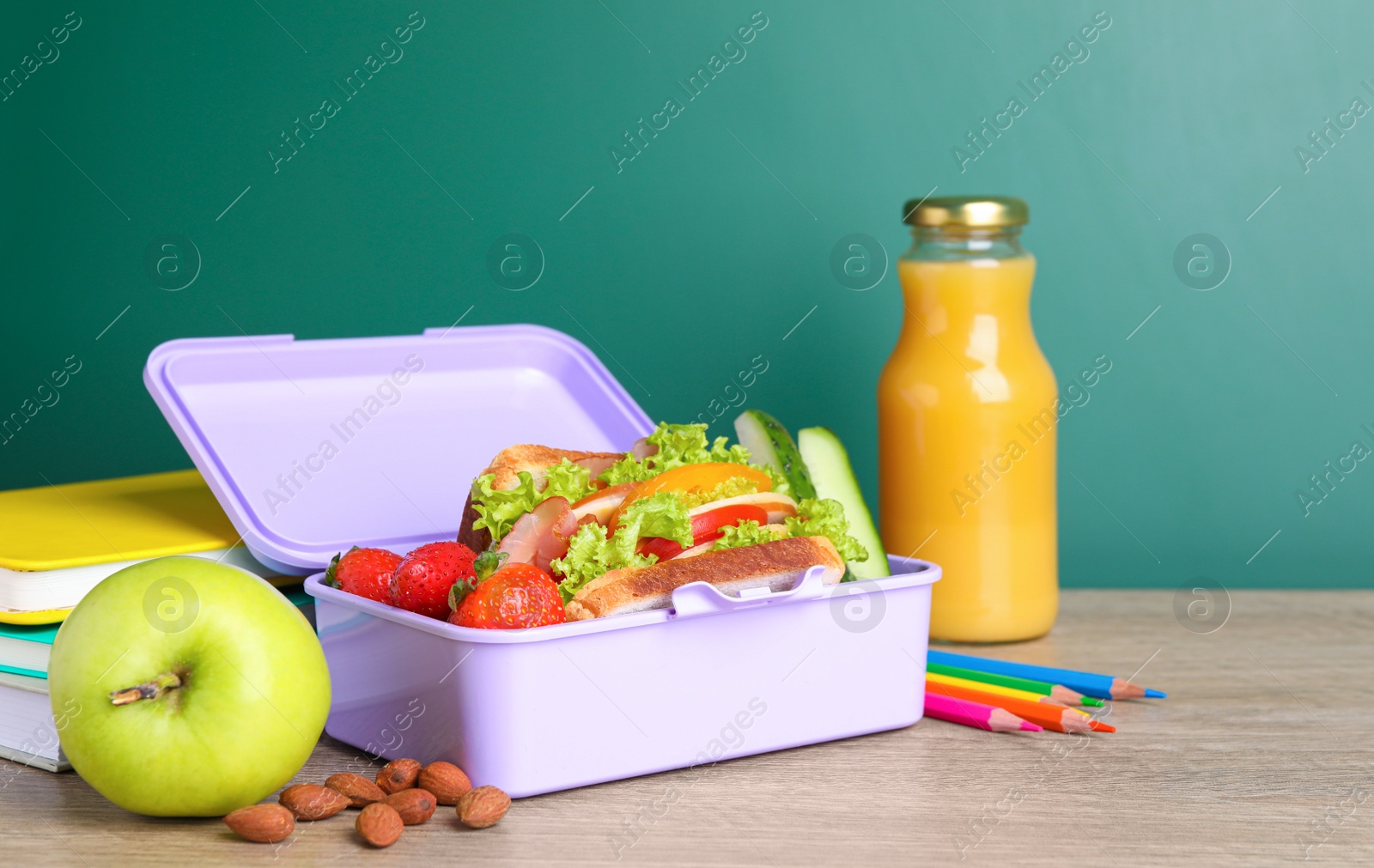 Photo of Lunch box with healthy food and different stationery on wooden table near green chalkboard
