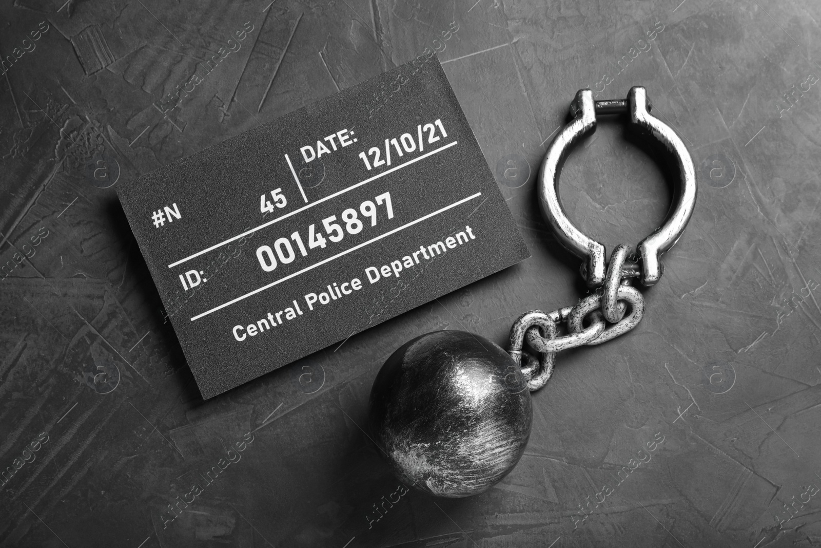 Photo of Metal ball with chain and mugshot letter board on grey table, flat lay