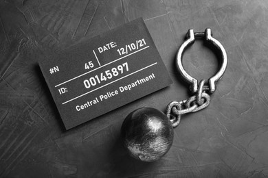 Photo of Metal ball with chain and mugshot letter board on grey table, flat lay
