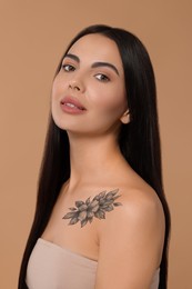 Young woman with beautiful floral tattoo on beige background