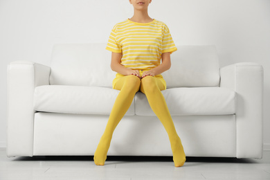 Woman wearing yellow tights sitting on sofa indoors, closeup