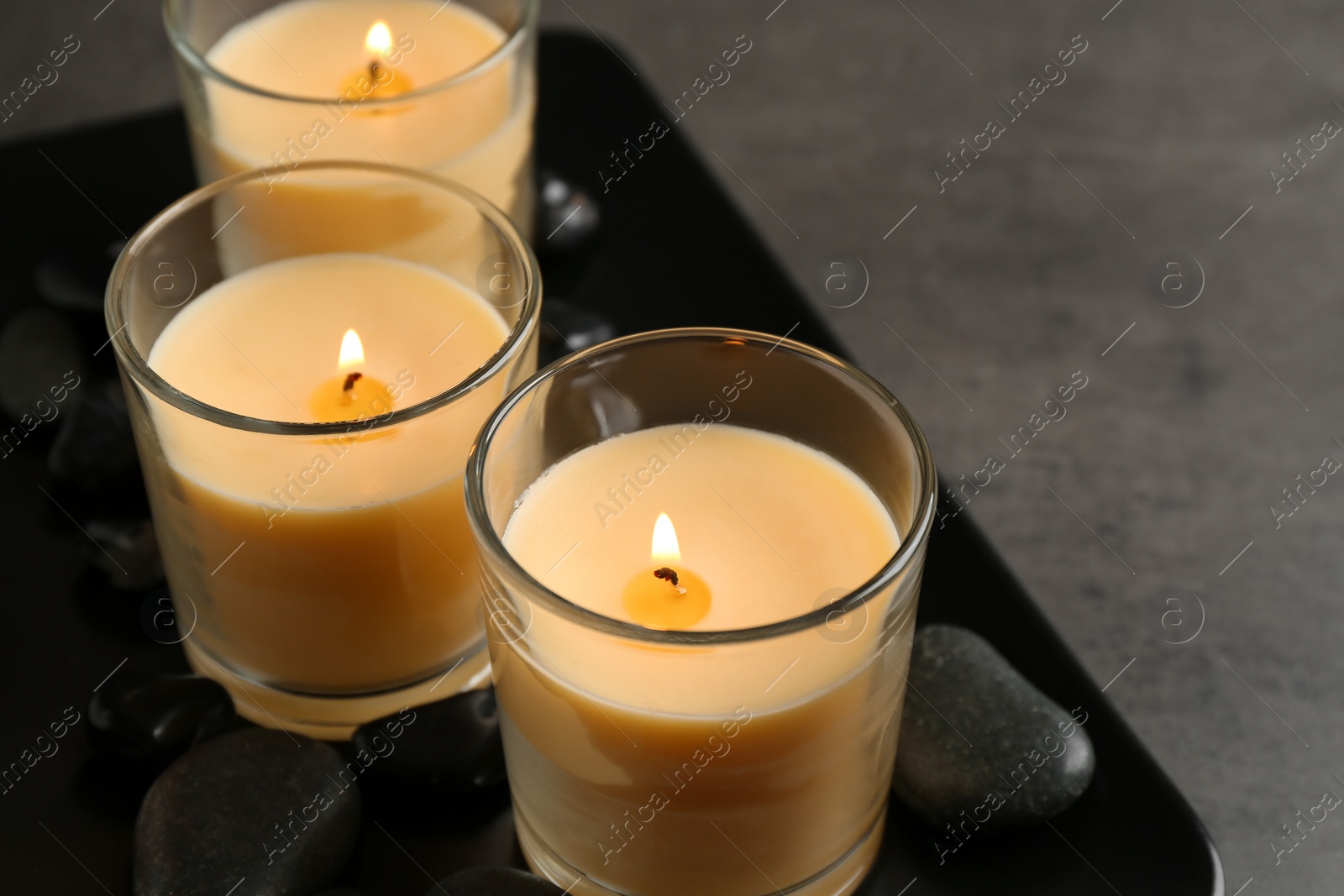 Photo of Dark plate with three burning candles on table. Space for text
