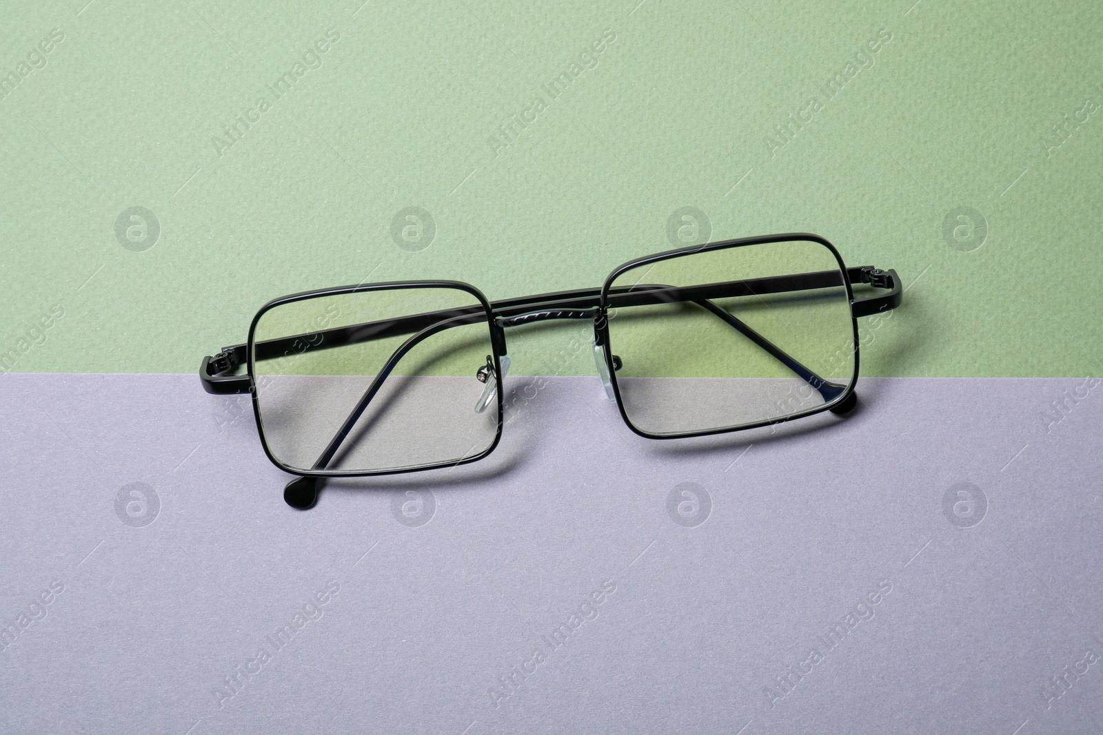 Photo of Stylish pair of glasses with black frame on color background, top view