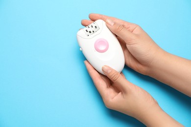 Woman holding modern epilator on light blue background, top view. Space for text