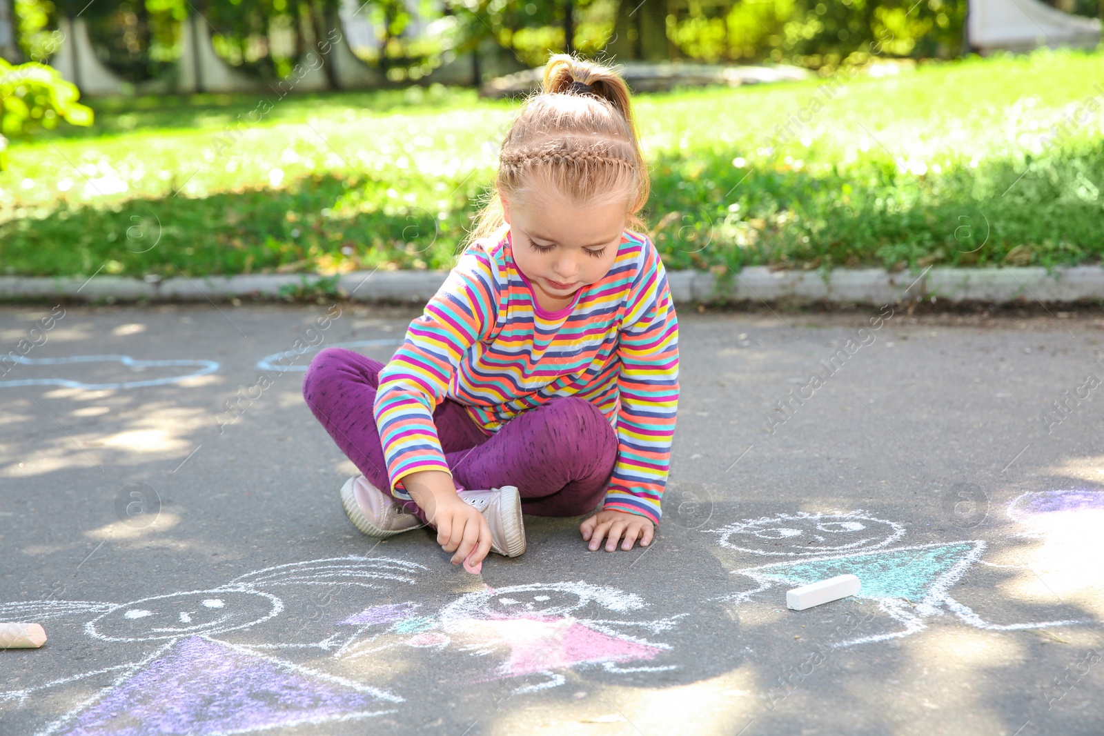 Photo of Little child drawing with colorful chalk on asphalt
