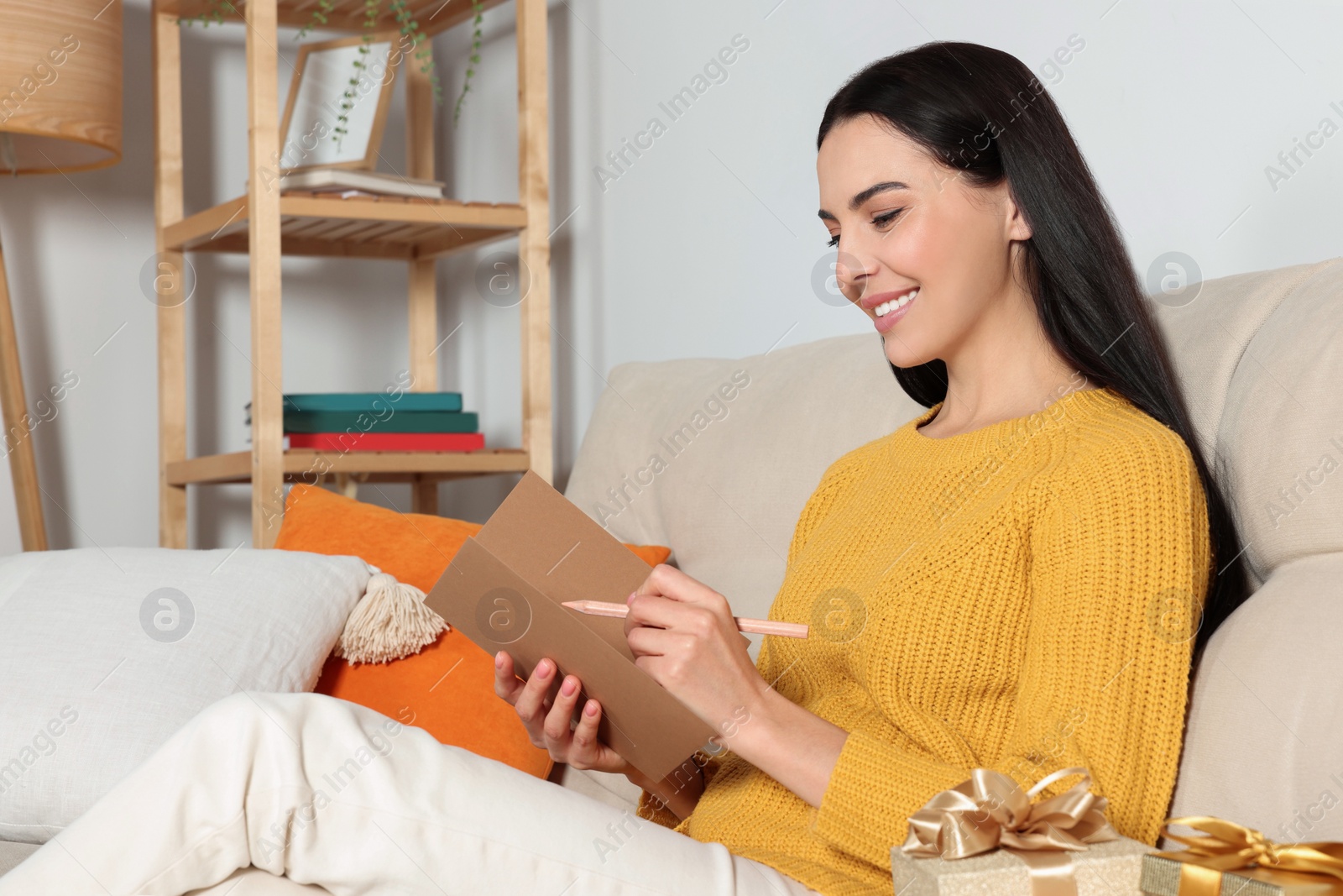 Photo of Happy woman reading greeting card on sofa in living room