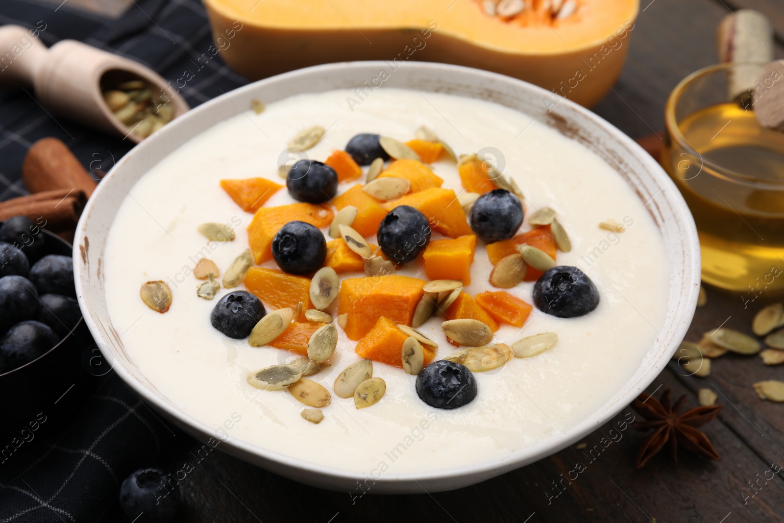 Photo of Bowl of delicious semolina pudding with blueberries, pumpkin and seeds on table, closeup