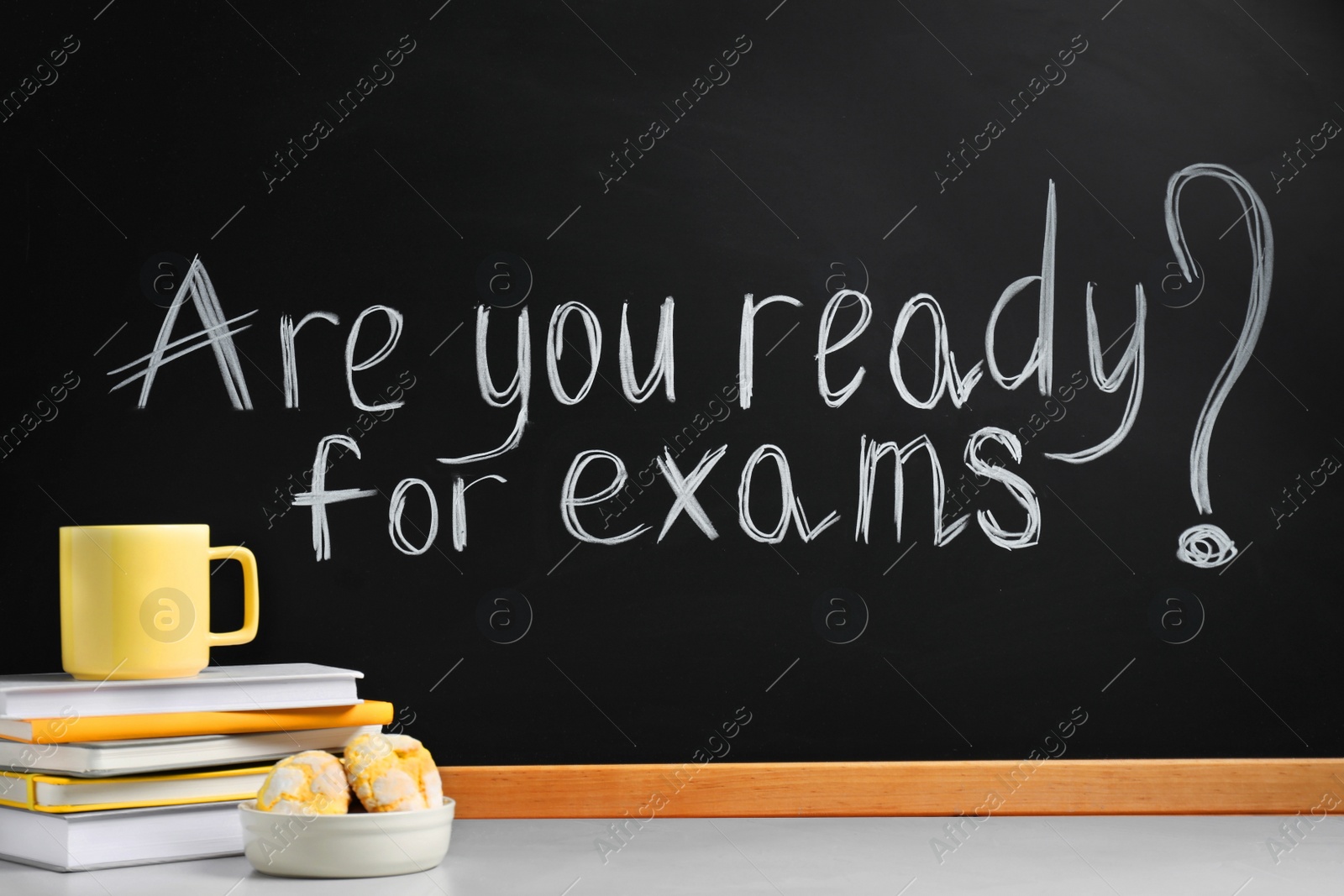 Photo of Different stationery, cup and cookies on light table near blackboard with phrase Are You Ready For Exams