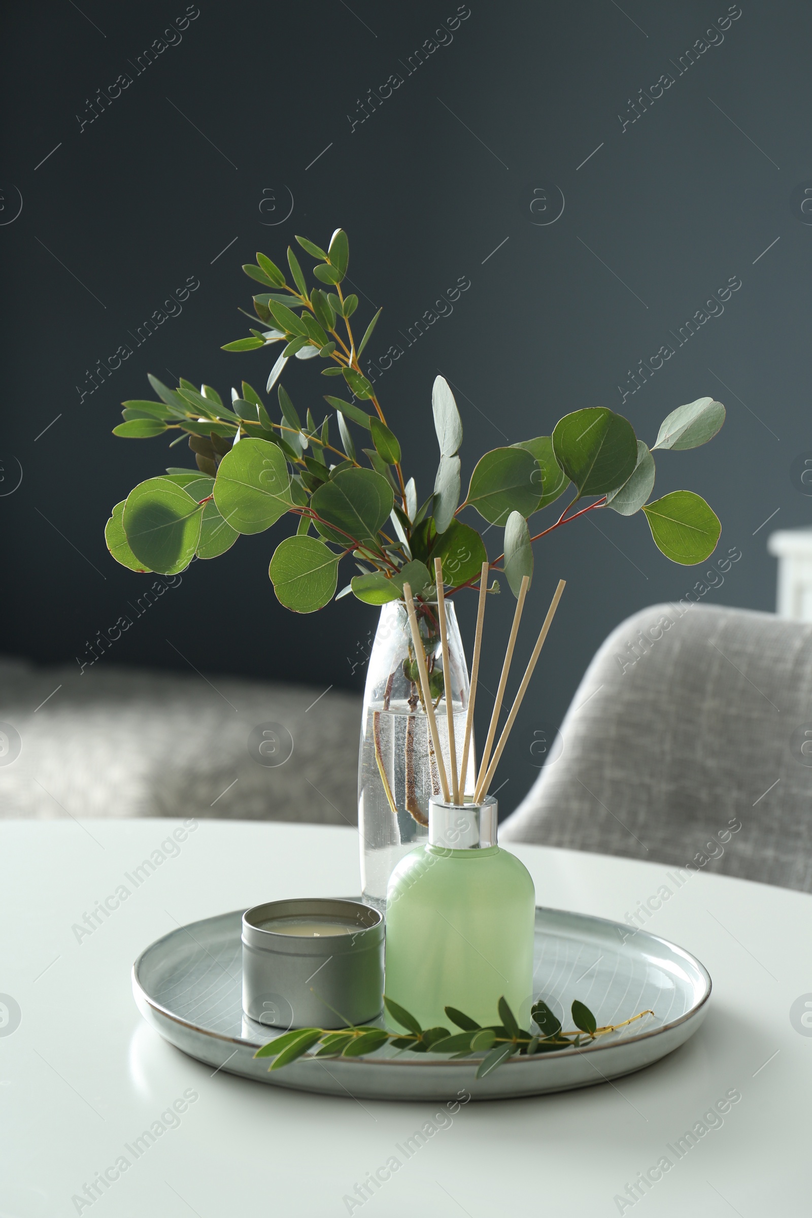 Photo of Eucalyptus branches, candle and aromatic reed air freshener on white table indoors. Interior elements