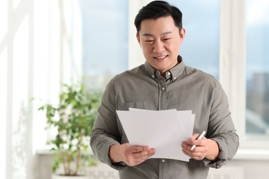 Portrait of smiling businessman with documents in office. Space for text