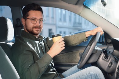 Photo of Coffee to go. Handsome man with paper cup of drink driving his car