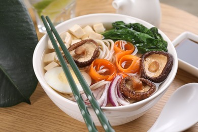 Photo of Delicious vegetarian ramen served on wooden table, closeup. Noodle soup