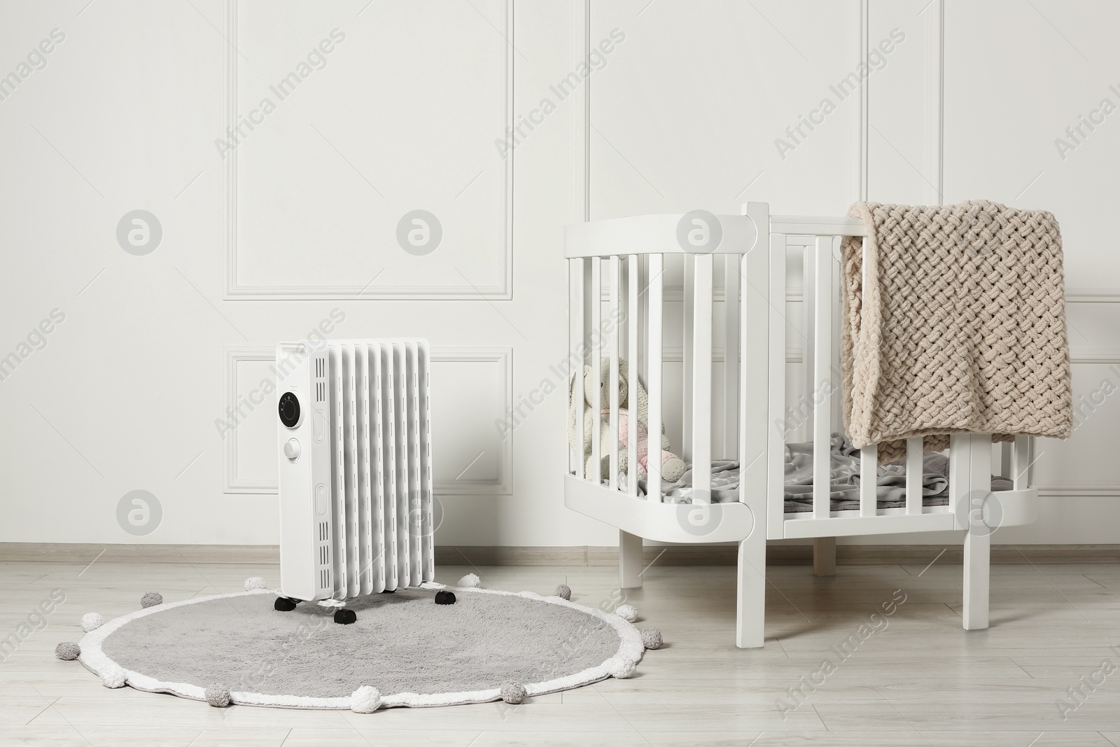 Photo of Modern portable electric heater on rug and baby crib indoors