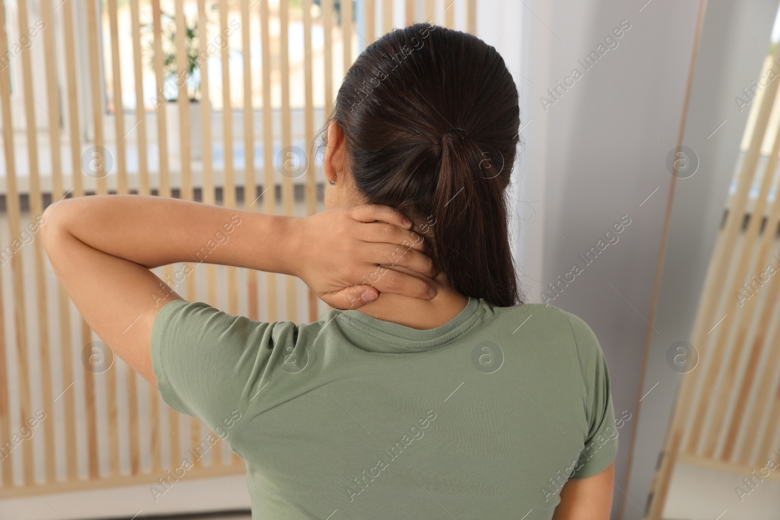 Photo of Young woman suffering from neck pain indoors, back view