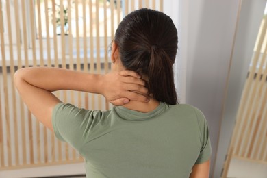 Young woman suffering from neck pain indoors, back view