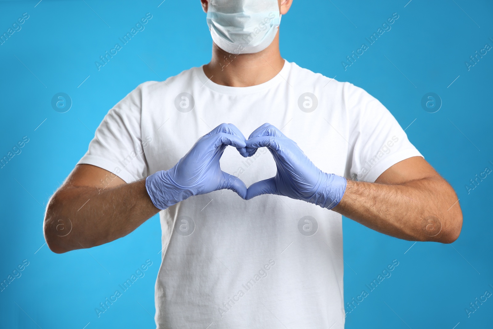 Photo of Man in protective face mask and medical gloves making heart with hands on blue background, closeup