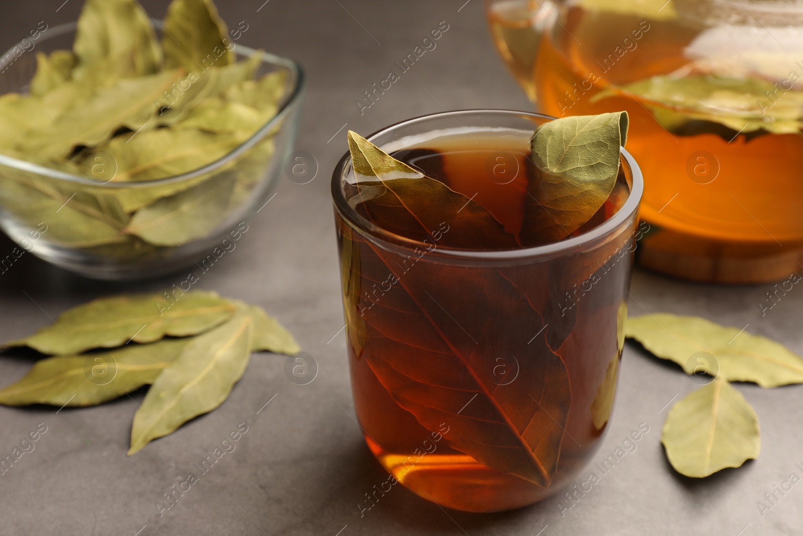 Photo of Cup of freshly brewed tea with bay leaves on grey table, closeup