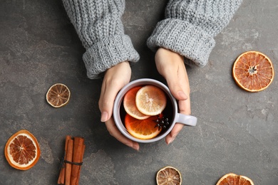Photo of Woman in warm sweater with cup of hot winter drink on gray background, top view. Cozy season