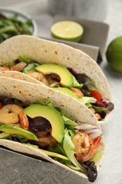 Photo of Delicious tacos with shrimps and avocado on light grey table, closeup