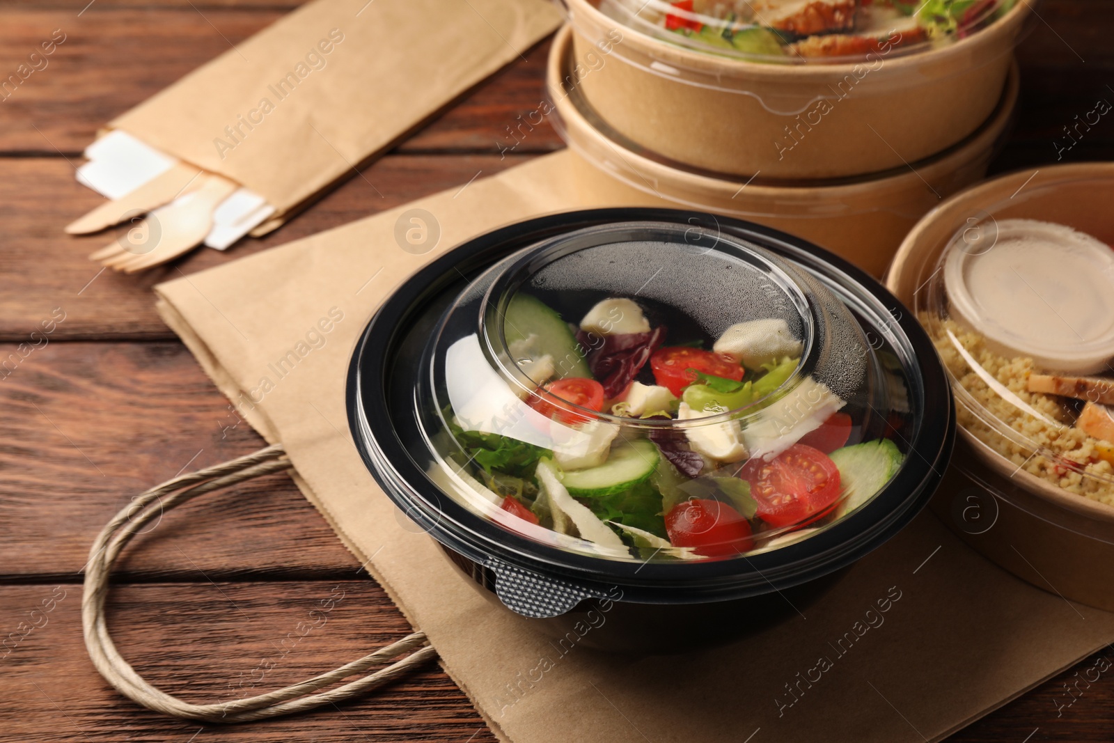 Photo of Tasty food in containers with knife and fork on wooden table