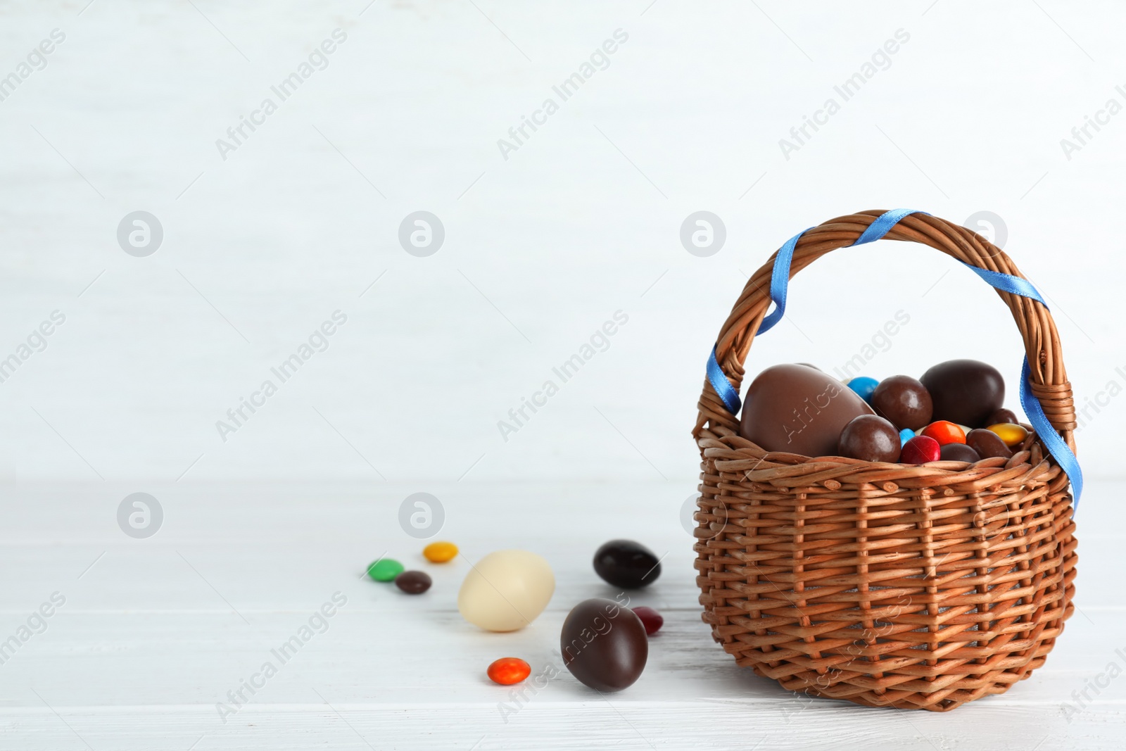 Photo of Composition with chocolate Easter eggs and wicker basket on table. Space for text