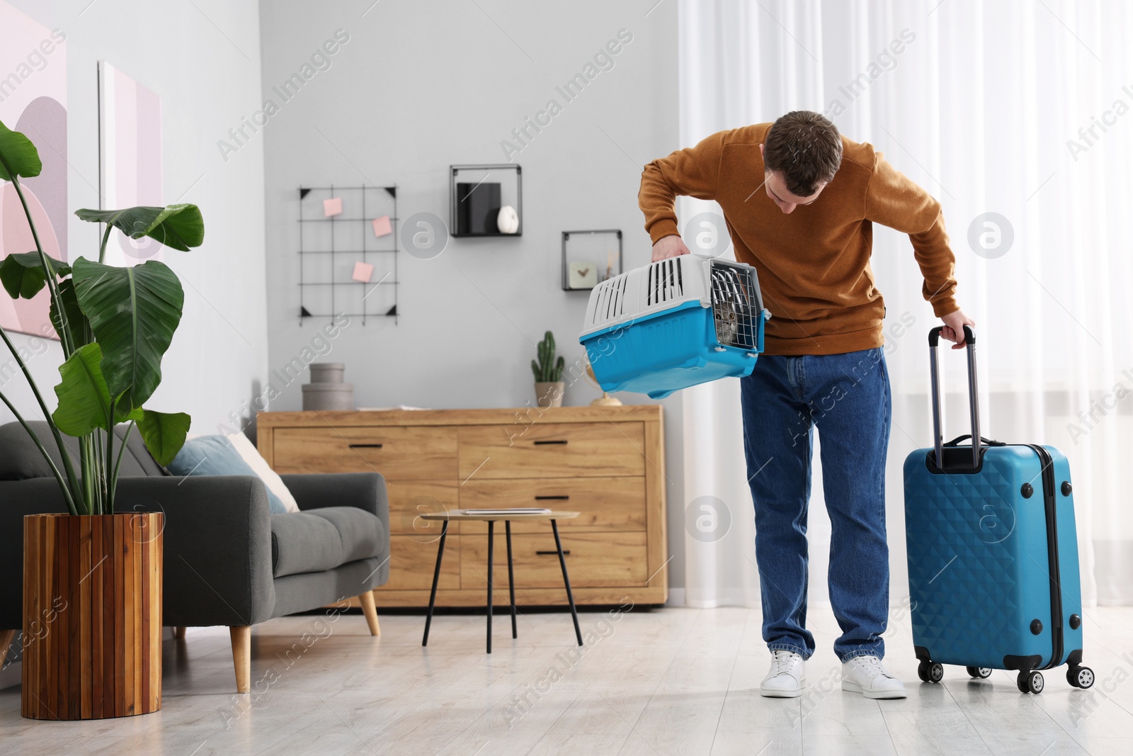 Photo of Travel with pet. Man holding carrier with cute cat and suitcase at home, space for text