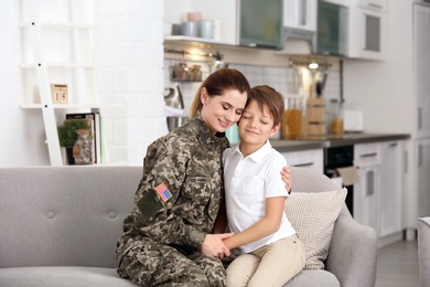 Woman in military uniform with her little son on sofa at home