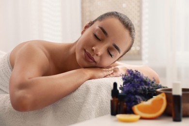Woman relaxing on massage couch and bottles of essential oil with ingredients on table in spa salon