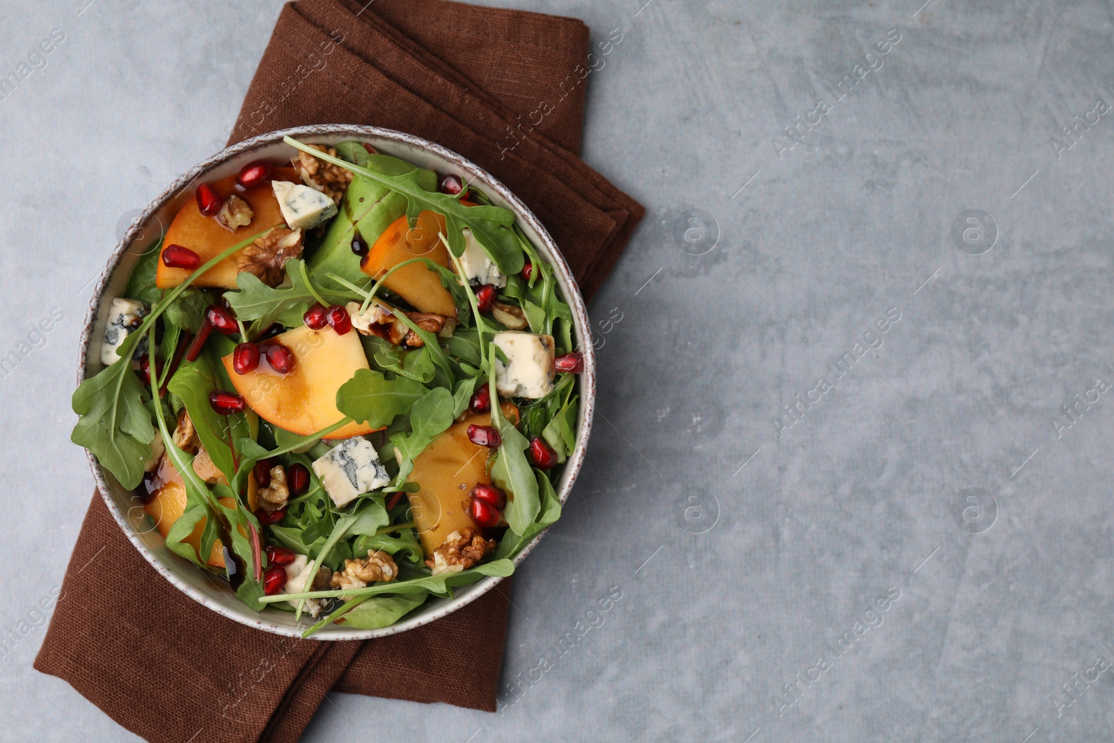 Photo of Tasty salad with persimmon, blue cheese, pomegranate and walnuts served on light grey table, top view. Space for text