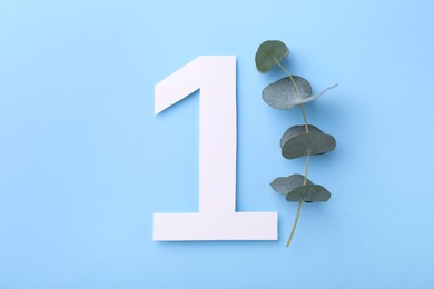Photo of Paper number 1 and eucalyptus branch on light blue background, top view