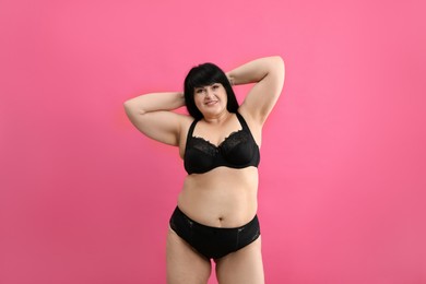 Photo of Beautiful overweight woman in black underwear on pink background. Plus-size model