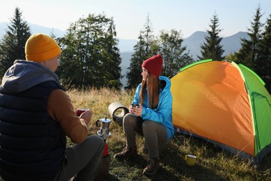 Young couple drinking coffee near camping tents in mountains