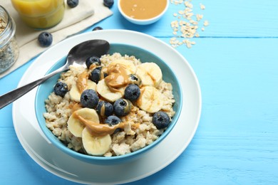 Photo of Tasty oatmeal with banana, blueberries and peanut butter served in bowl on light blue wooden table, space for text