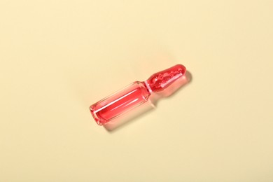 Photo of Glass ampoule with liquid on beige background, top view