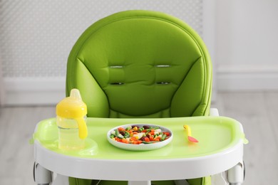 Photo of Baby high chair with healthy food and water indoors