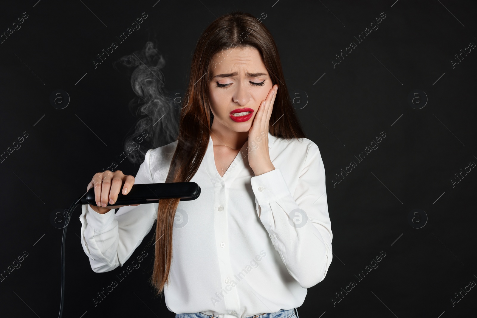 Photo of Upset young woman with flattening iron on black background. Hair damage