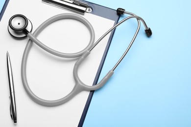 Photo of Clipboard with stethoscope and pen on light blue background, top view. Space for text