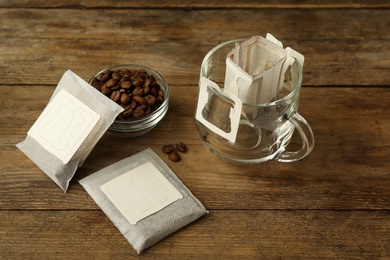 Photo of Drip coffee bags, beans and glass cup on wooden  table
