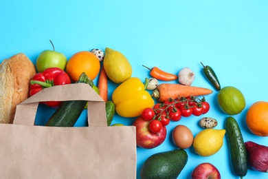 Photo of Paper bag with different groceries on light blue background, flat lay