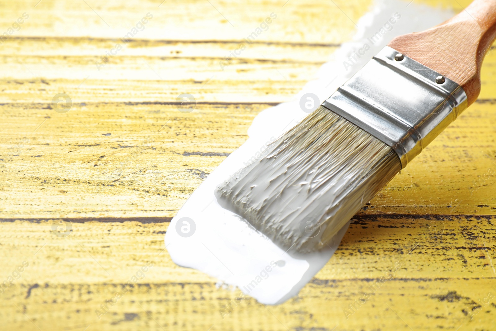 Photo of Paint stroke and brush on yellow wooden table, closeup. Space for text