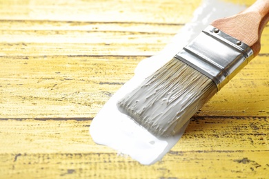 Photo of Paint stroke and brush on yellow wooden table, closeup. Space for text