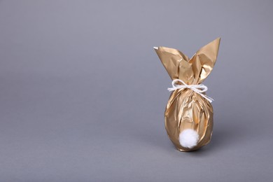 Photo of Easter bunny made of shiny gold paper and egg on grey background. Space for text