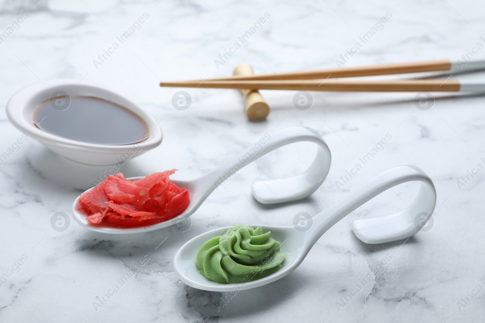 Photo of Swirl of wasabi paste, pickled ginger, soy sauce and chopsticks on white marble table