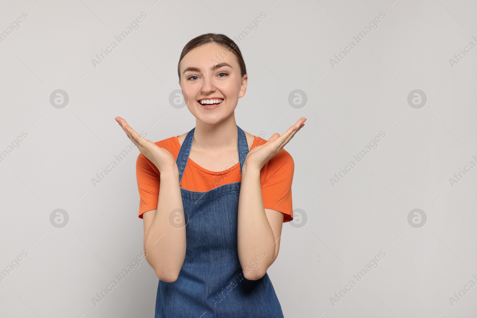 Photo of Beautiful young woman in clean denim apron on light grey background