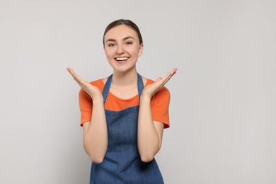 Beautiful young woman in clean denim apron on light grey background