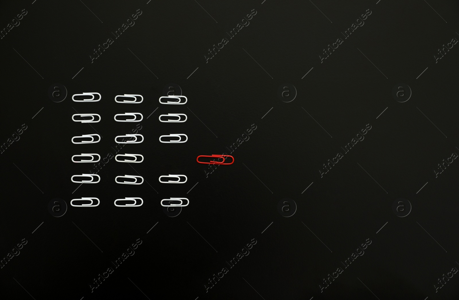 Photo of White paper clips following after red one on black background, flat lay. Space for text