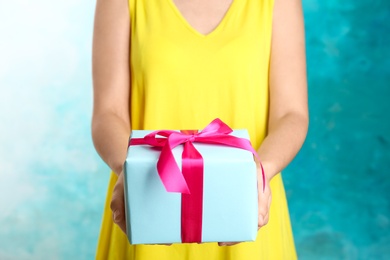 Photo of Woman holding beautifully wrapped gift box on color background