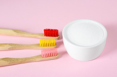 Photo of Bamboo toothbrushes and bowl with baking soda on pink background