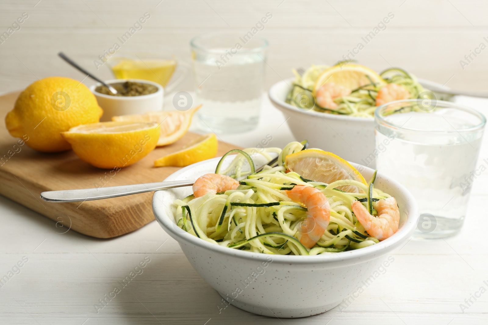 Photo of Delicious zucchini pasta with shrimps and lemon in bowl served on white wooden table