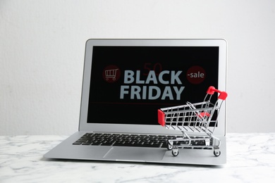 Photo of Laptop and small cart on white marble table. Black Friday Sale online